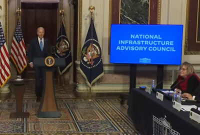 A man is standing in from of National Infrastructure Advisory Council at The White House to speak about American Infrastructure.